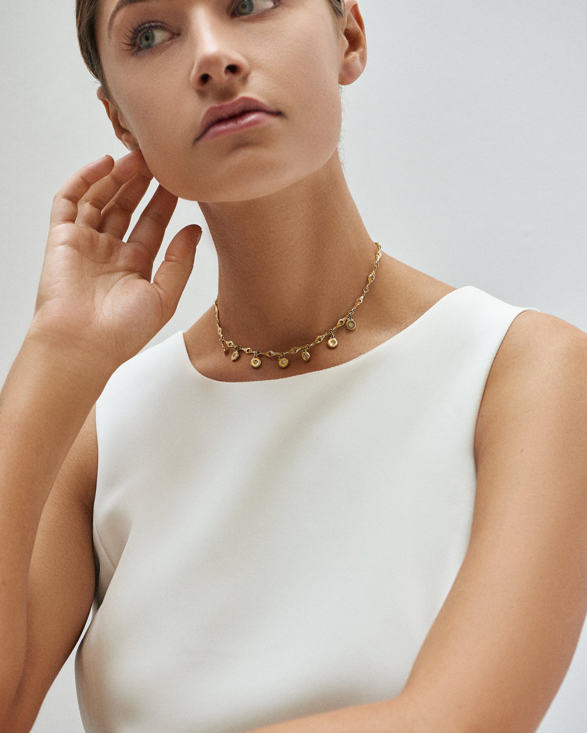 A woman in a white sleeveless top wearing a short Ilene Joy medallion necklace
