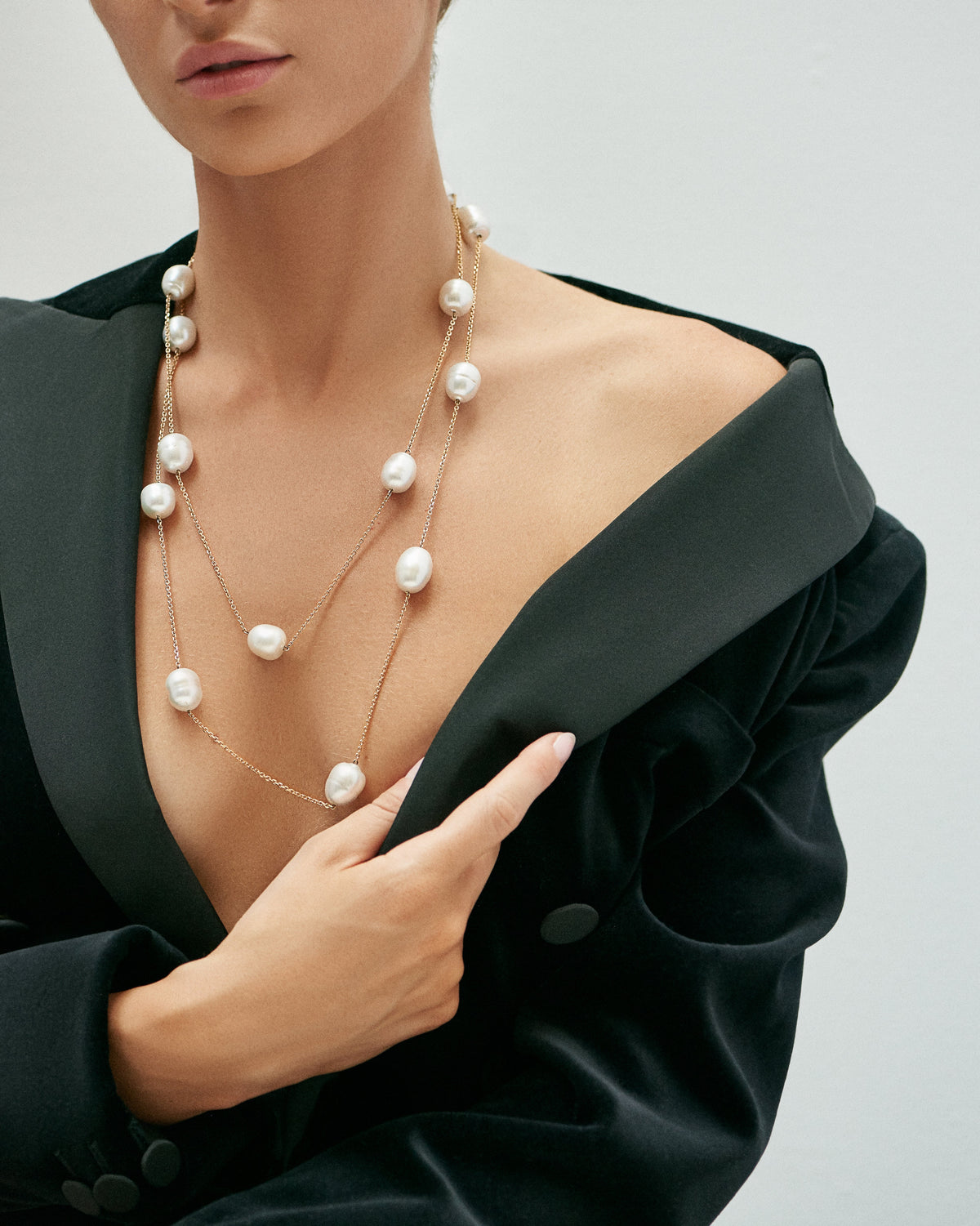 A woman in a black blazer wearing the Chain Reaction Pearl Necklace in gold