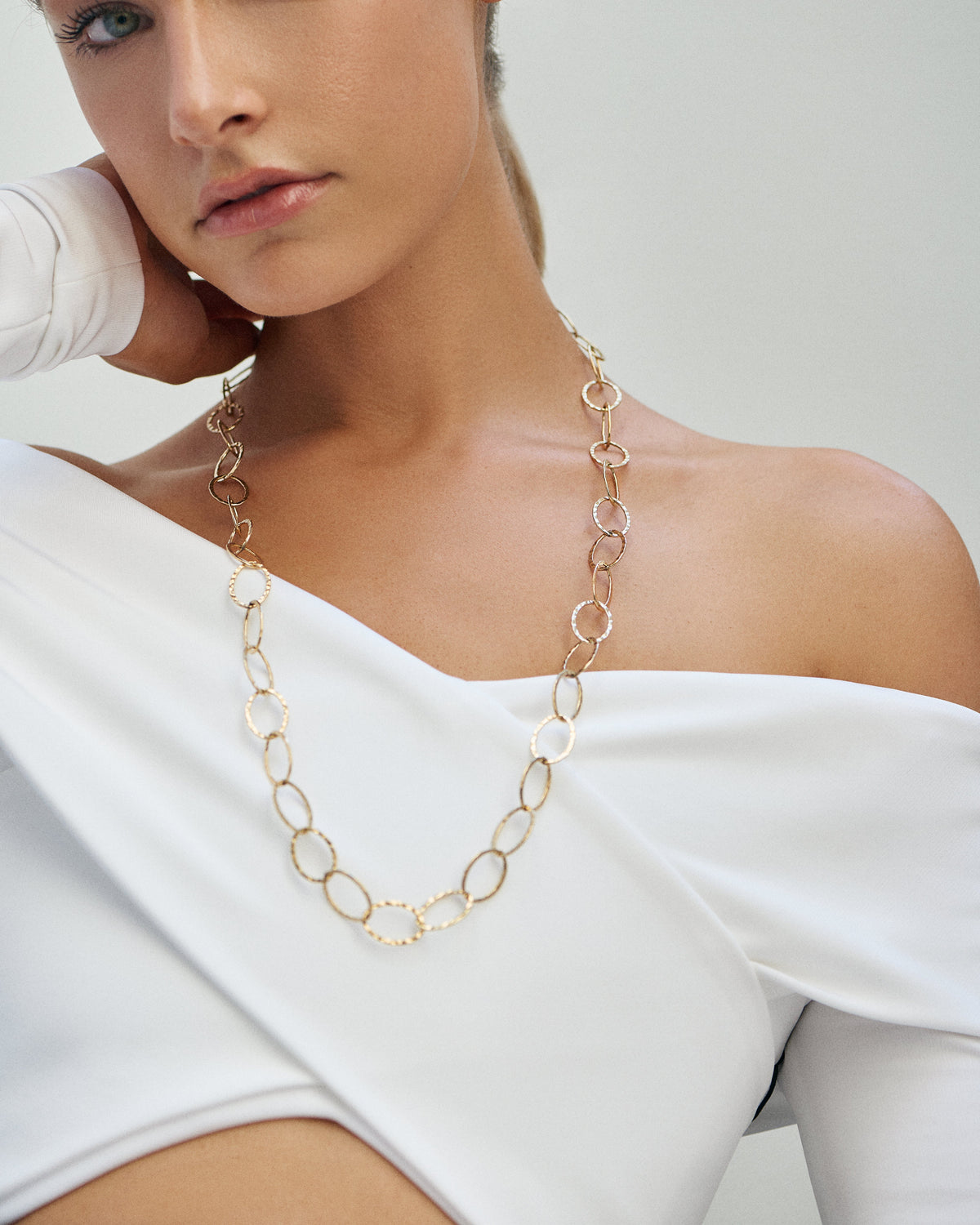 A woman in a white off-the-shoulder top wearing a long hammered gold circle chain necklace