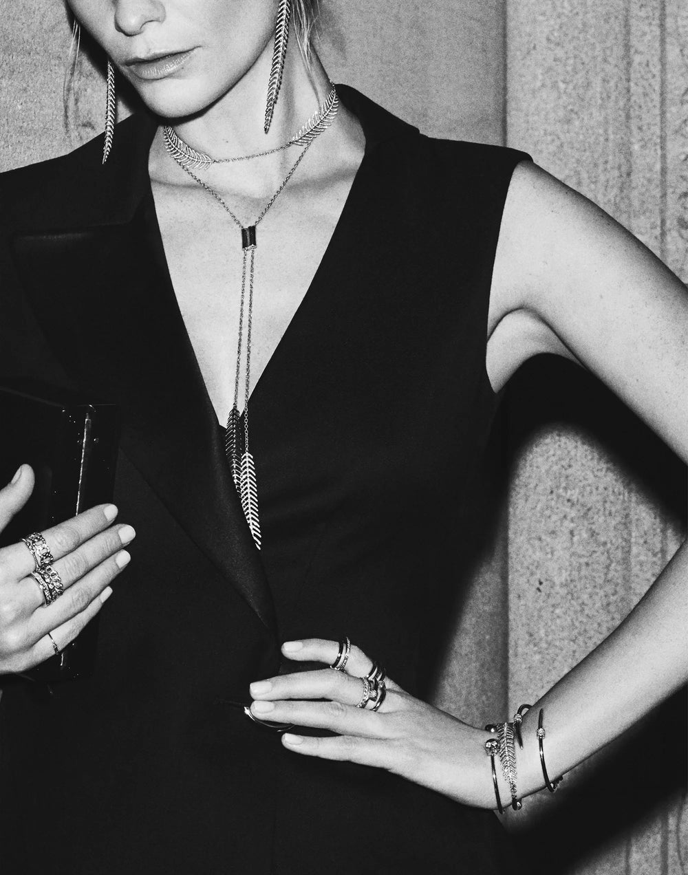 Black and white photograph of a woman in a black sleeveless dress wearing long Ilene Joy necklaces and stacked rings
