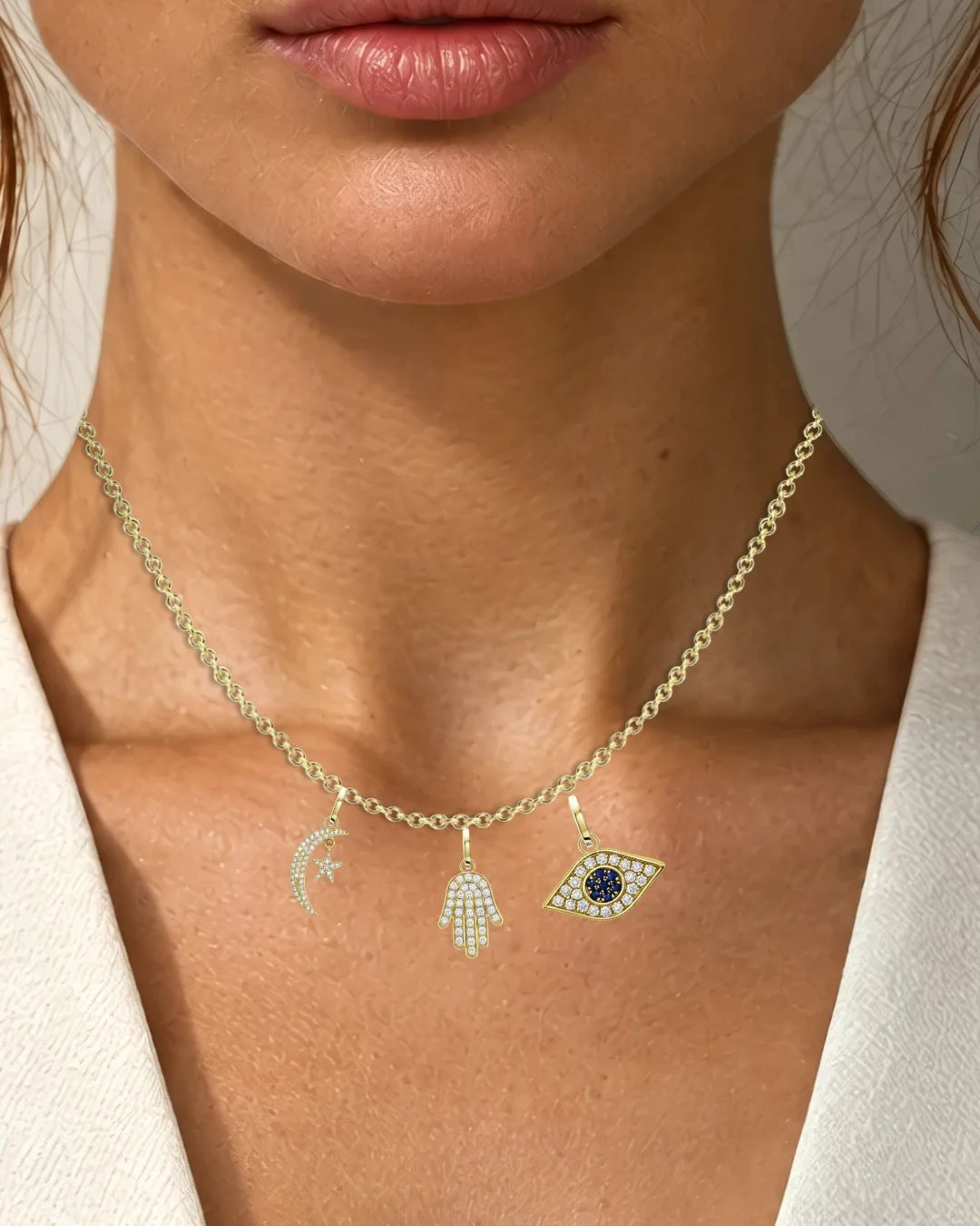 A fine gold chain at the neck with a crescent, a pavé hamsa and an eye charm